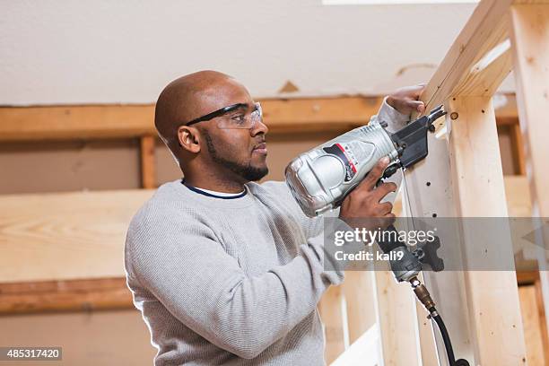 negro trabajador de construcción con pistola de clavos - herramienta eléctrica fotografías e imágenes de stock