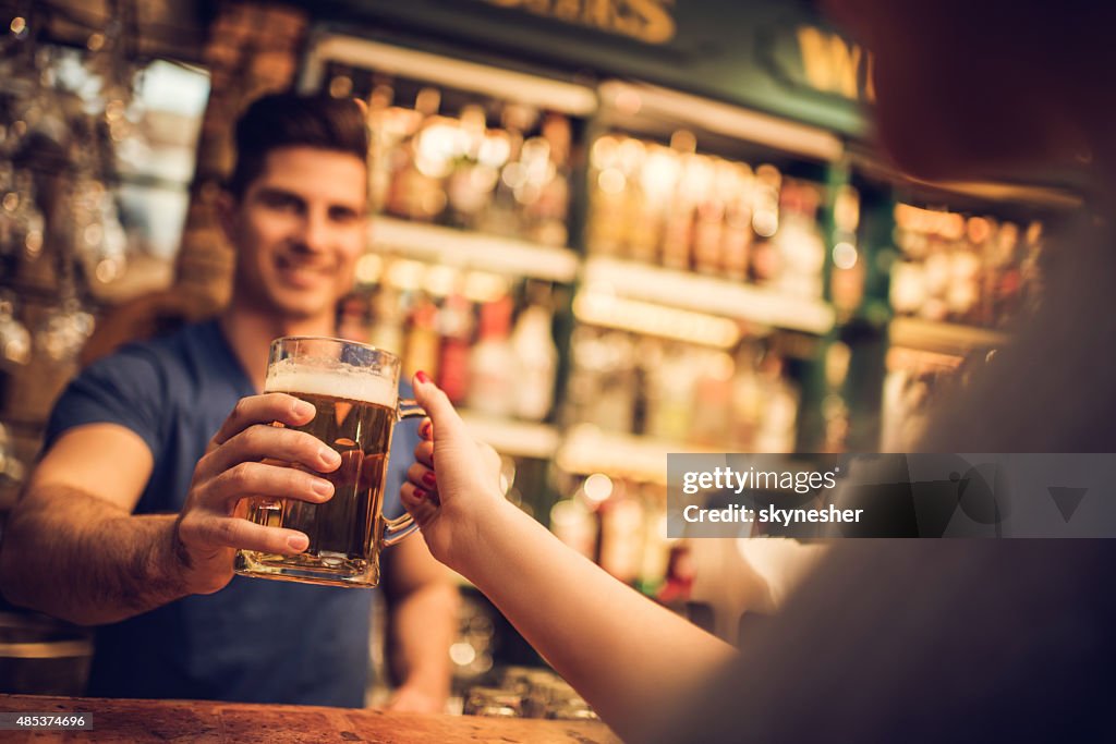 Close-up of bartender giving beer to a customer in bar.