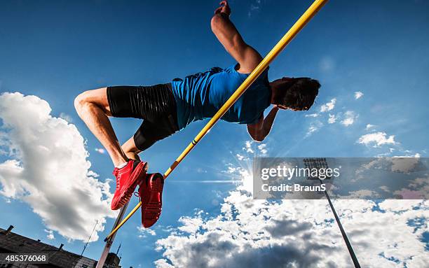 low angle view of a young man performing high jump. - womens high jump stock pictures, royalty-free photos & images