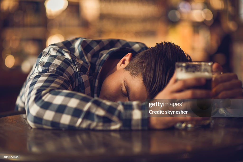 Young drunk man sleeping on the table in a bar.