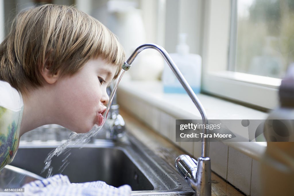 Young boy drinking water from tap