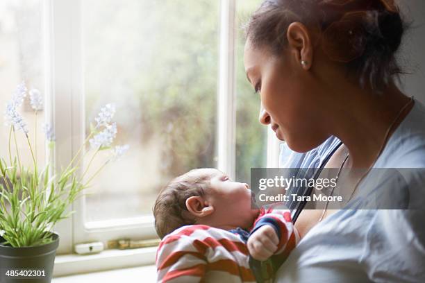 mother holding baby by window - leanincollection family stock pictures, royalty-free photos & images