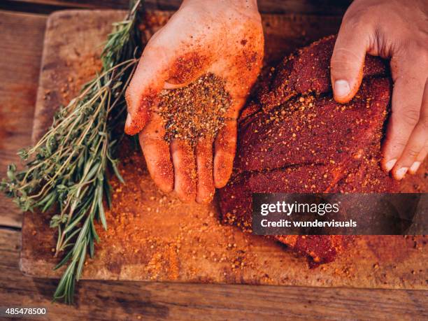 hand mit pikanten gewürzen mit einem stück schweinefleisch mit schnittkanten - schwein grill stock-fotos und bilder