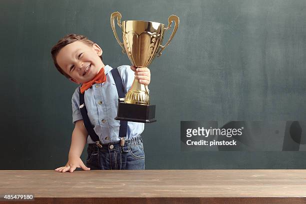 little boy raising a golden trophy - trophy award stock pictures, royalty-free photos & images