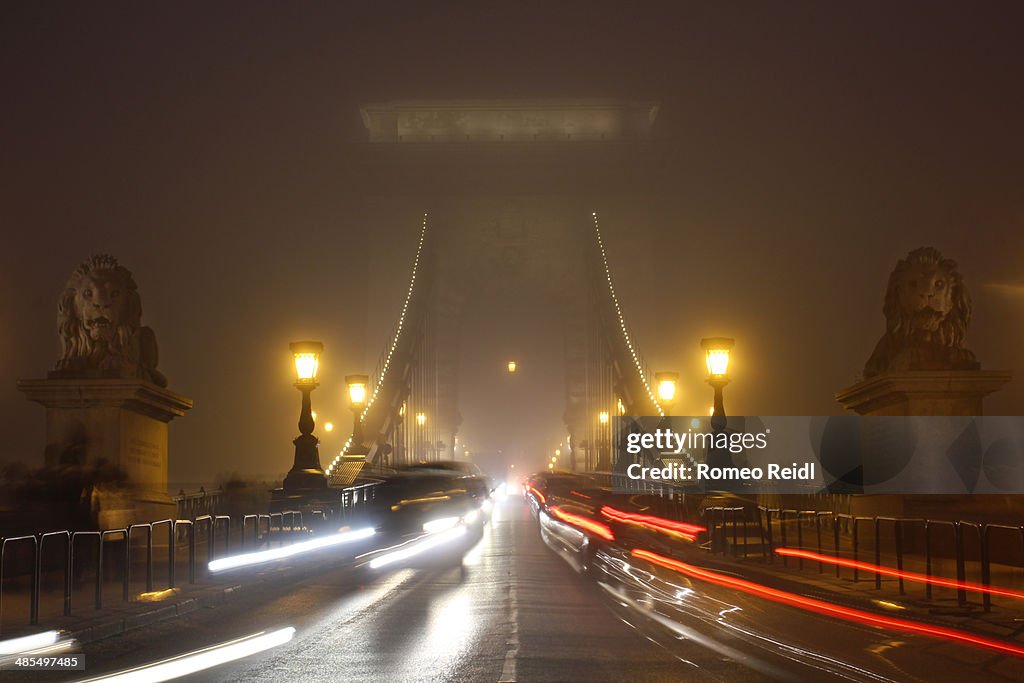 Foggy chain bridge entrance at night with traffic