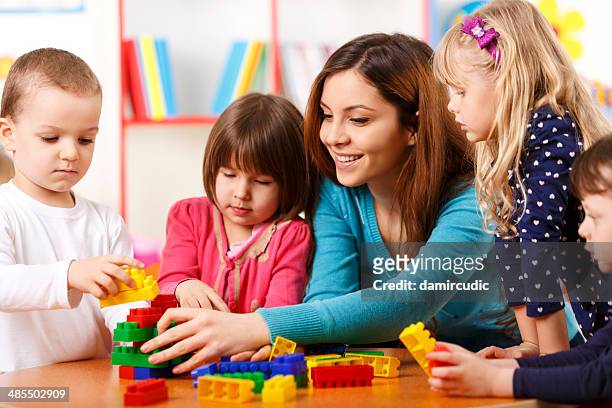 nursery teacher and preschoolers playing with building blocks - nanny stock pictures, royalty-free photos & images