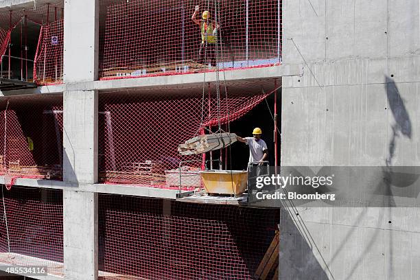 Builders move building material into a skip while working on a social housing site, under development by Spanish construction company Sacyr SA in...