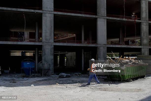 Builder walks past a building skip filled with timber as it sits on a social housing site, under development by Spanish construction company Sacyr SA...