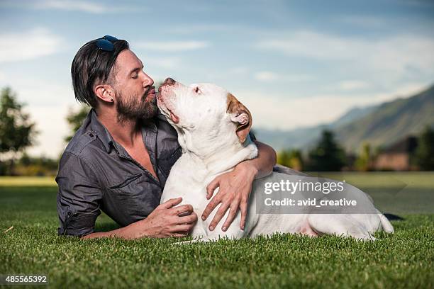 affectionate pet owner kisses his dog outdoors - american bulldog stock pictures, royalty-free photos & images