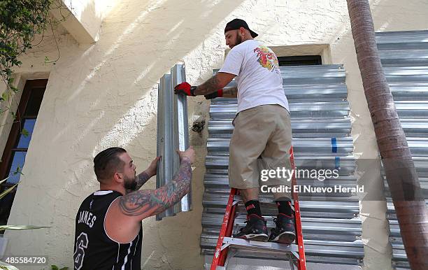 From left, Joe's Stone Crab employees Jordan Garcia and Manny Cortes installing shuttles in preparation for Tropical Storm Erika on Friday, August 28...