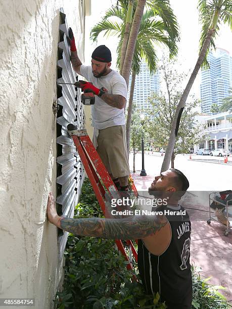 Joe's Stone Crab employees Jordan Garcia, top, and Manny Cortes installing shuttles in preparation for Tropical Storm Erika on Friday, August 28 in...