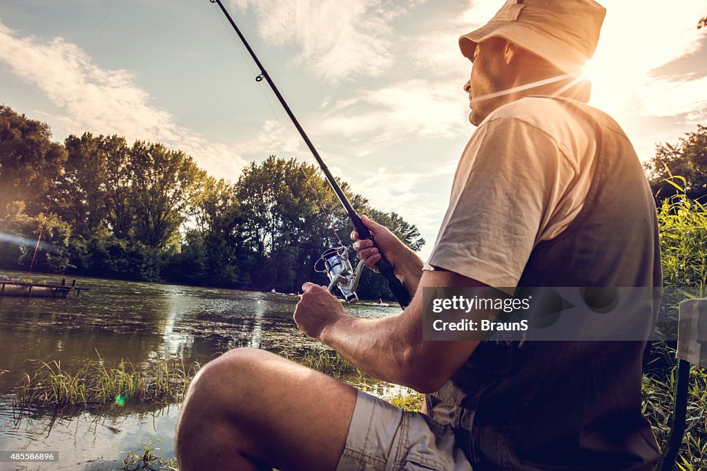 Mid adult fisherman river fishing at sunset.