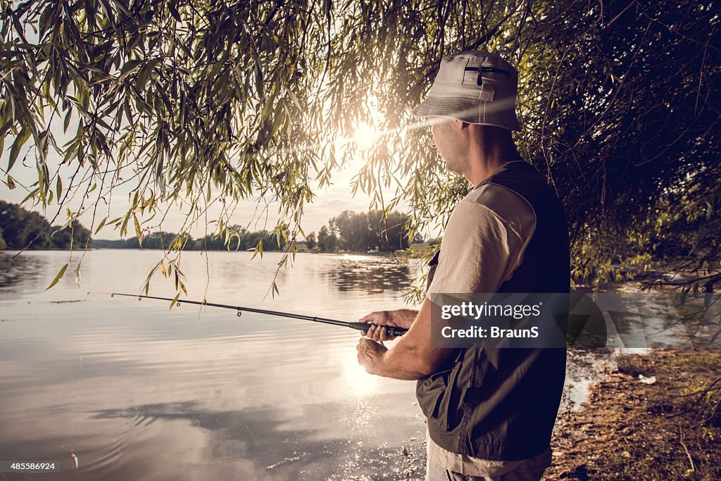 Man spending his free time in river fishing at sunset.