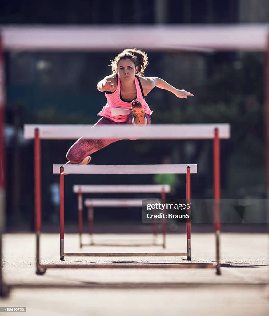 Determined female athlete jumping hurdles on a race.