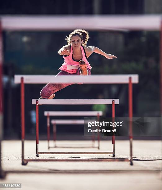 determined female athlete jumping hurdles on a race. - hurdle stock pictures, royalty-free photos & images