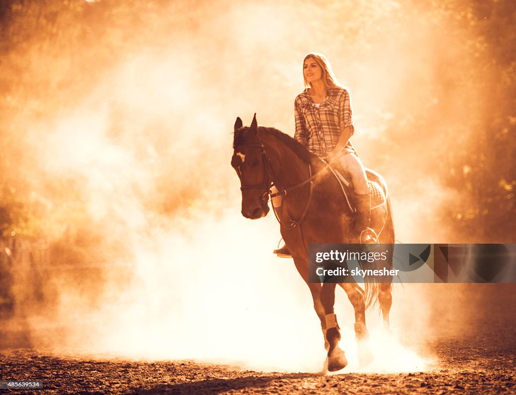 Young woman horseback riding at sunset.