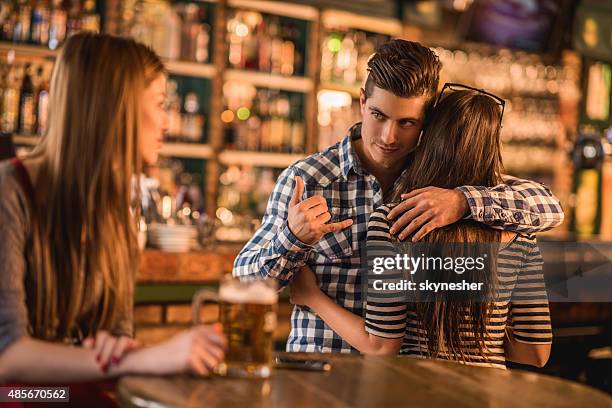 unfaithful young man making call gesture in a cafe. - affari stock pictures, royalty-free photos & images