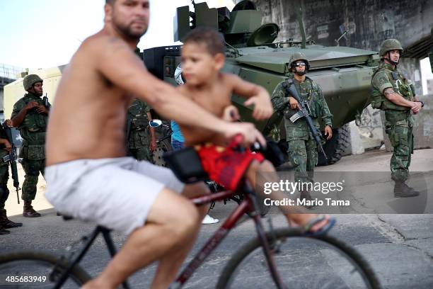 Brazilian soldiers keep watch as a man and boy bike past in the occupied Complexo da Mare, one of the largest 'favela' complexes in Rio, on April 19,...