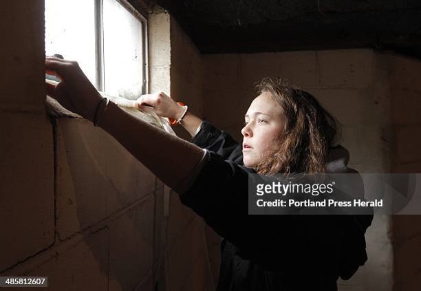 Gregory Rec/Staff Photographer -- Jenna Gardiner, a senior at The New School in Kennebunk, applies weatherstripping to a basement window in a home in...