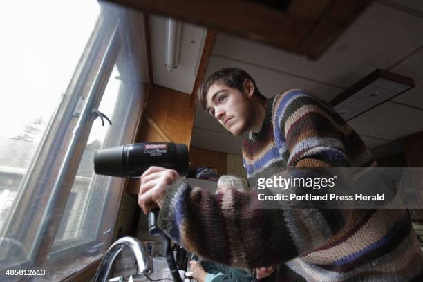 Gregory Rec/Staff Photographer -- Senior Nick Schmid uses a hair dryer to apply shrink-wrap to a kitchen window at a home in Kennebunk. --