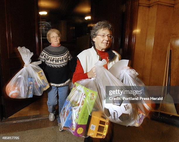John Ewing/Staff Photographer -- Volunteers Judy Calise, left, of Cape Elizabeth, and Julie Pew of Yarmouth carry bags of toys for families waiting...