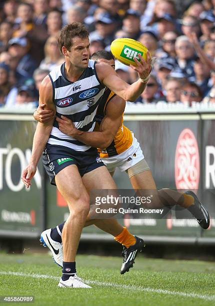 Jared Rivers of the Cats handballs whilst being tackled by Paul Puopolo of the Hawks during the round five AFL match between the Geelong Cats and the...
