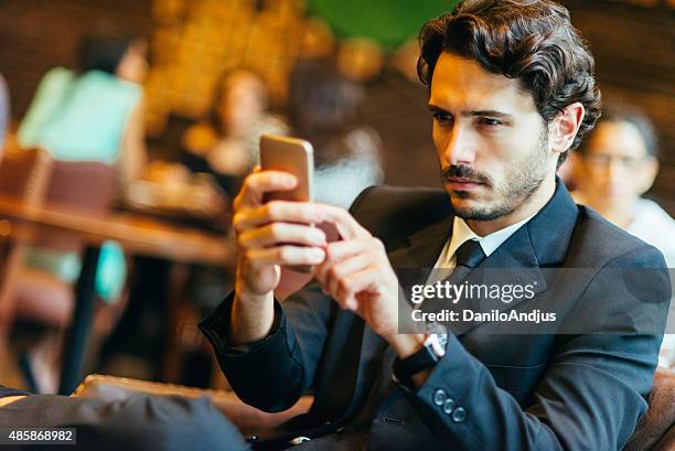 handsome businessman typing text message while relaxing in the bar - blue suit stock pictures, royalty-free photos & images