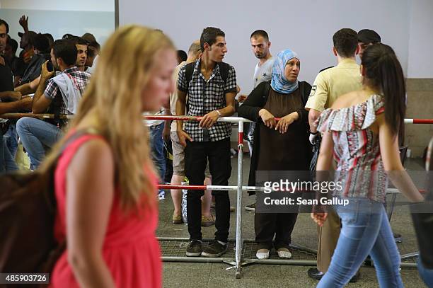 Travellers walk past migrants standing in a holding area who had arrived by train at Munich Hauptbahnhof main railway station and were detained by...