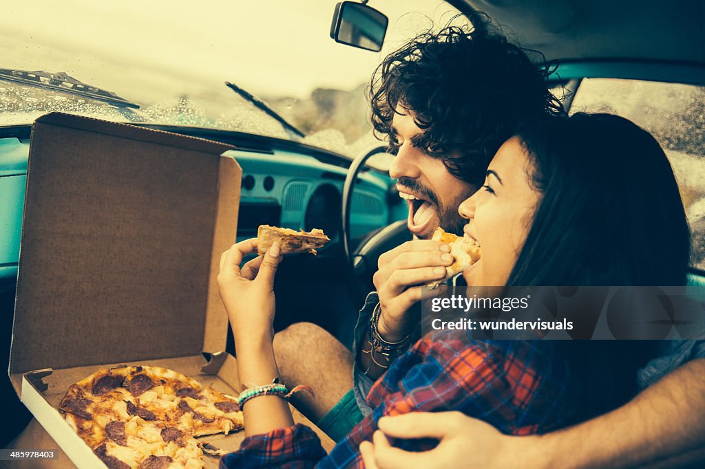 Couple eating pizza in retro car