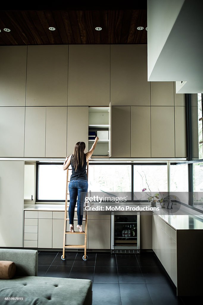 Woman on ladder looking in cabinet