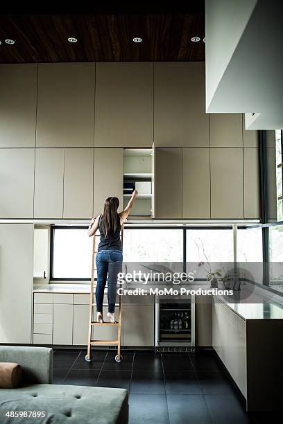 woman on ladder looking in cabinet - cabinet stock pictures, royalty-free photos & images