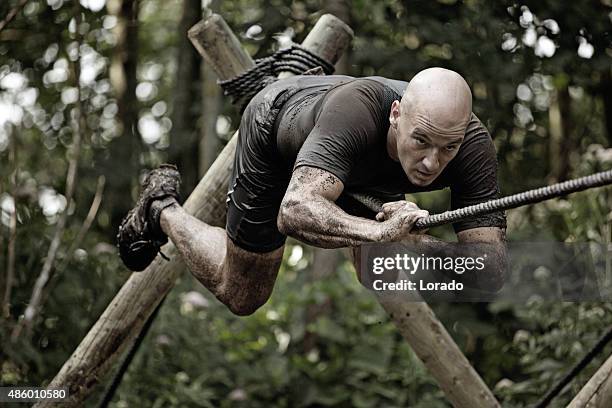 man climbing rope over mud obstacle - boot camp stock pictures, royalty-free photos & images