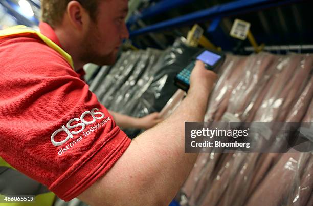 Worker uses a handheld device to scan an item of clothing as he prepares a customer order at Asos Plc's distribution warehouse in Barnsley, U.K., on...