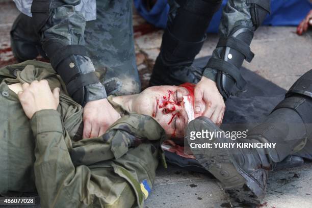 Police officers help a wounded colleague during clashes with activists of few radical Ukrainian parties in front of the parliament in Kiev on August...