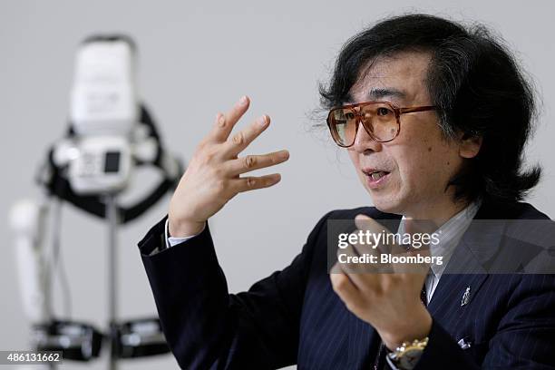 Yoshiyuki Sankai, founder and president of Cyberdyne Inc., gestures as he speaks in front of the lower-limb model Hybrid Assistive Limb exoskeleton...