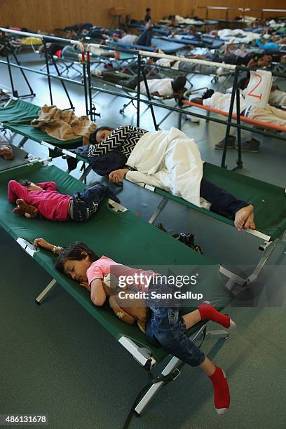 Migrants, including a mother and children from Afghanistan , who had arrived by train to Germany sleep on cots while waiting to register at a center...