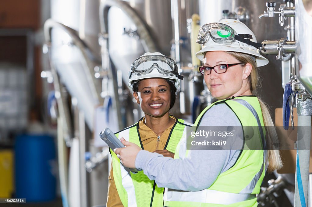 Two women working in a factory wearing hardhats