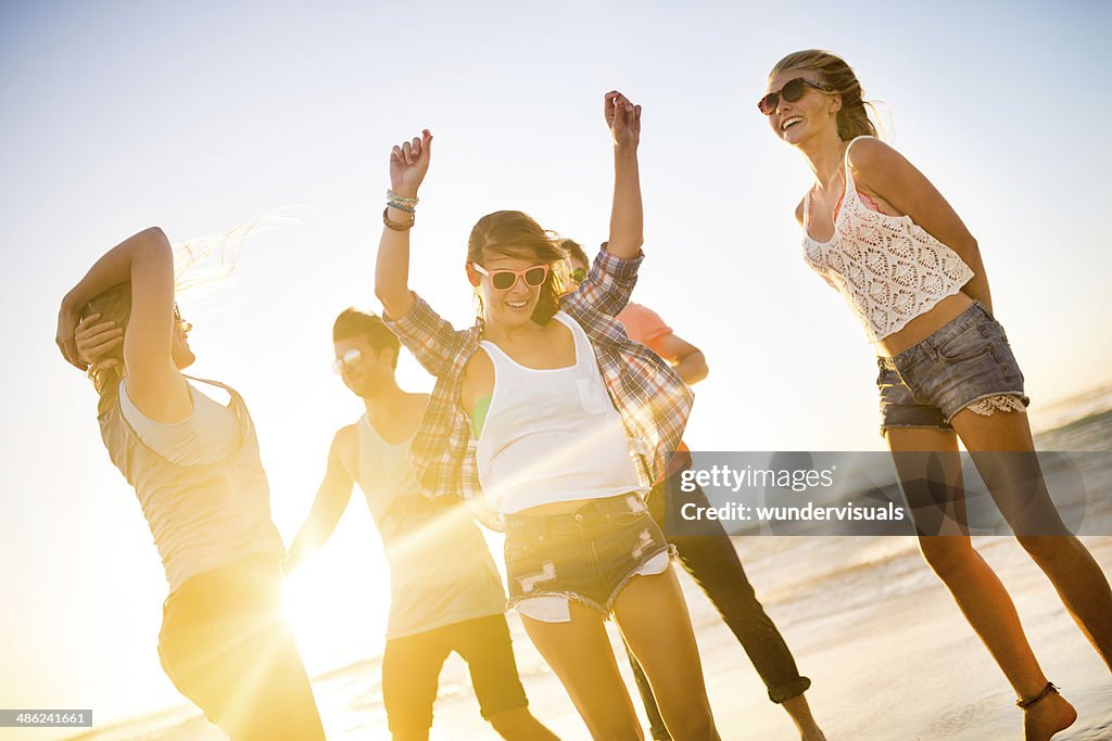 Friends dancing on beach in sunset