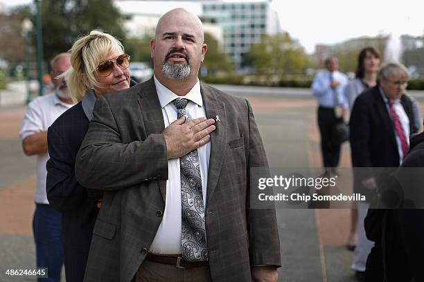 Consumer advocate Erin Brockovich leans on breast cancer survivor Mike Partain as he recites the Pledge of Allegiance during a small rally on Capitol...