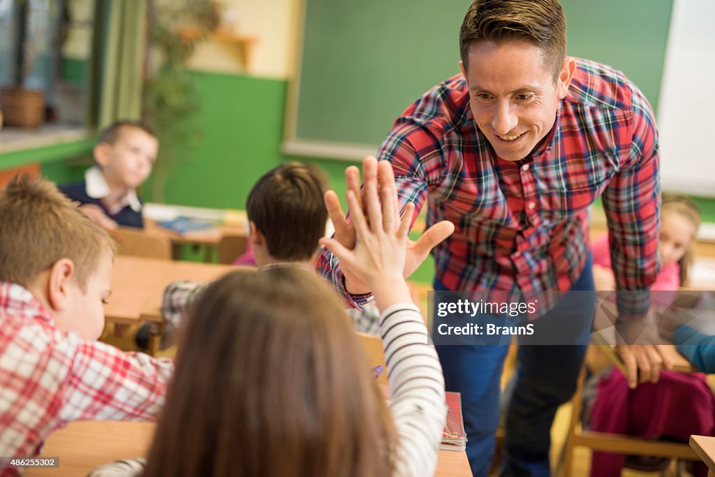 Happy elementary teacher congratulating his student on good answer.
