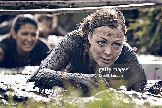 gruppe von frauen krabbeln in schlamm - assault courses stock-fotos und bilder