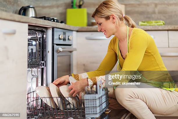 smiling woman using dishwasher in the kitchen. - loading dishwasher stock pictures, royalty-free photos & images