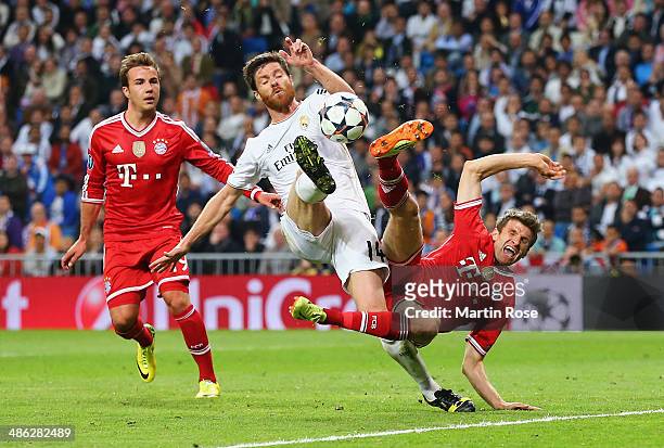 Xabi Alonso of Real Madrid challenges Thomas Mueller of Bayern Muenchen watched by Mario Goetze of Bayern Muenchen during the UEFA Champions League...