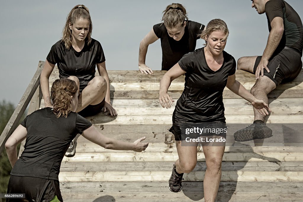 Male coach helping women to cross wooden wall obstacle
