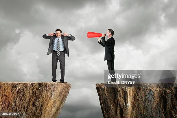 businessman shouting at another businessman through a megaphone - vingers in de oren stockfoto's en -beelden