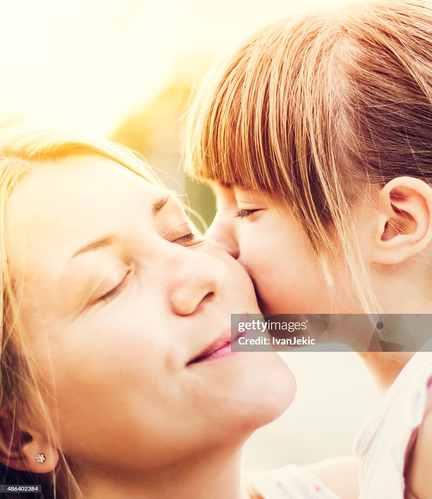 Young daughter kissing mother outdoors closeup