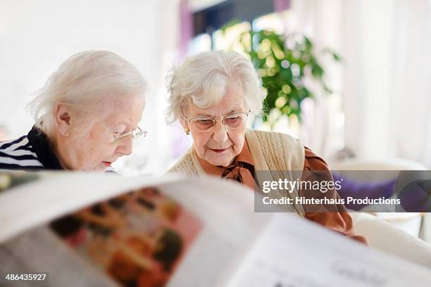 two senior woman reading newspaper - alleen seniore vrouwen stockfoto's en -beelden
