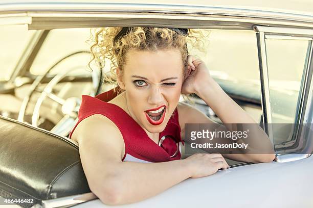 1950s woman winking at the camera in a vintage car - rockabilly stockfoto's en -beelden