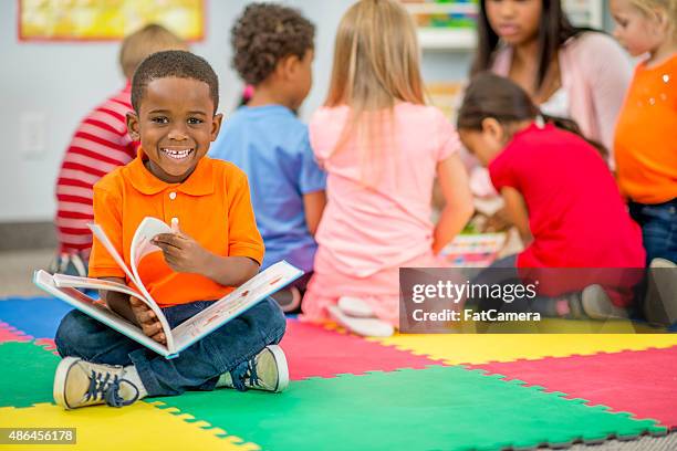 kleiner junge schaut bilderbuch im vorschulalter - boy reading a book stock-fotos und bilder