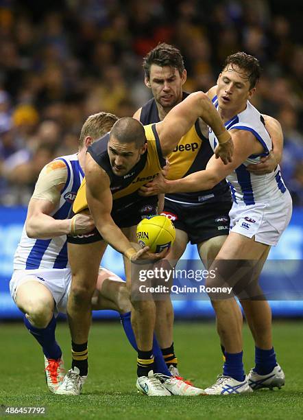 Shaun Grigg of the Tigers handballs whilst being tackled by Jack Ziebell of the Kangaroos during the round 23 AFL match between the Richmond Tigers...